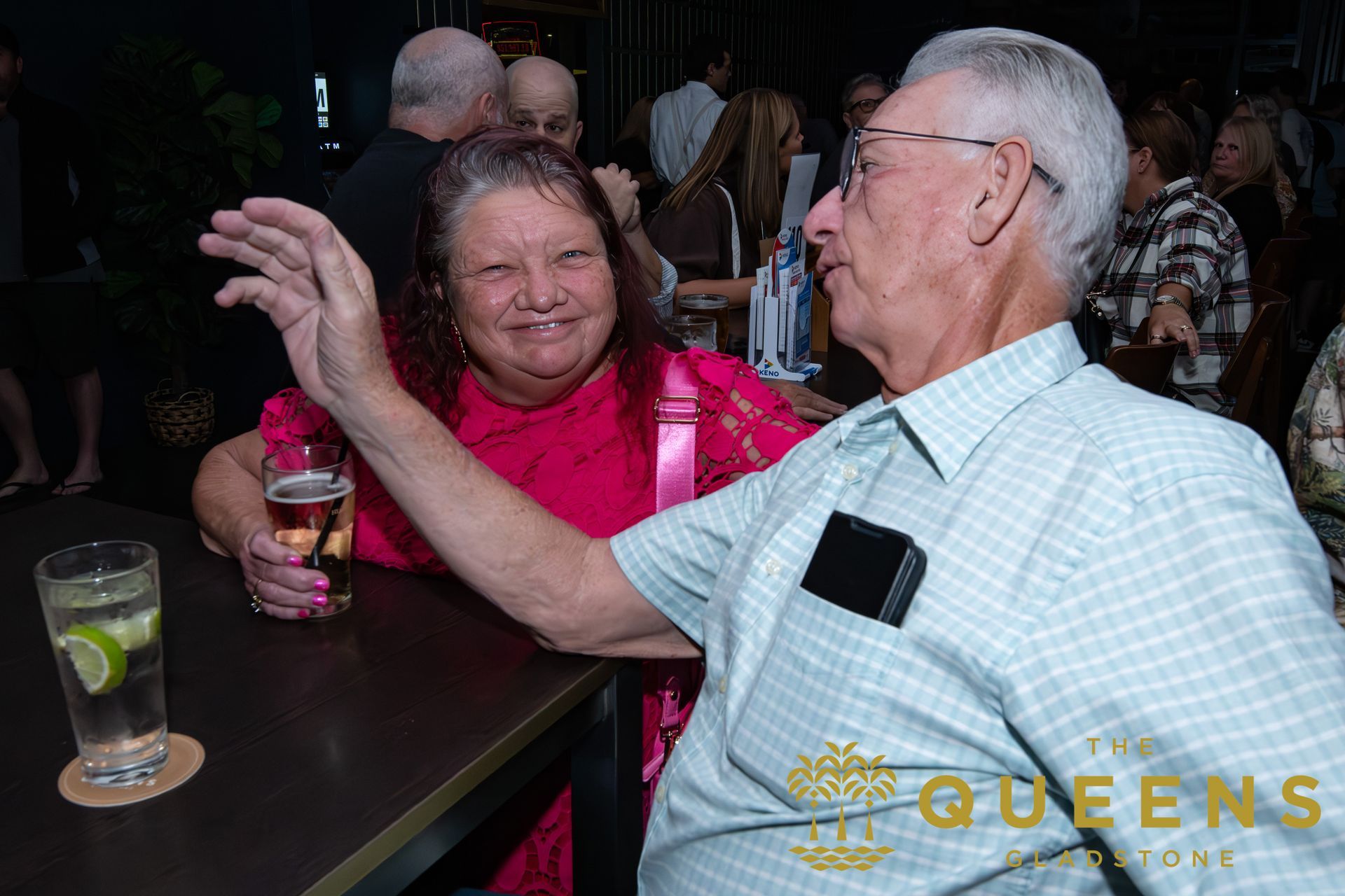 Two people chatting at a table, smiling with drinks in a dim indoor setting.