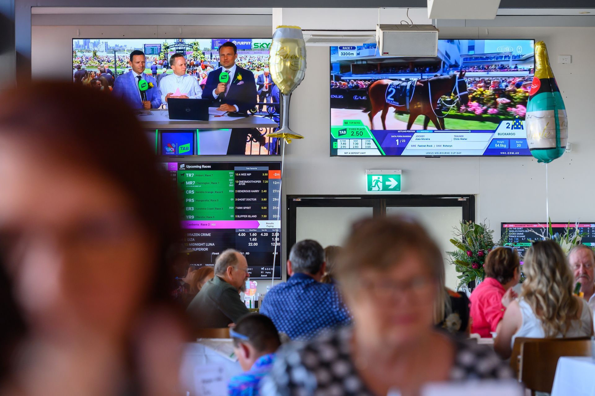 A group of people are sitting at tables in front of a large screen.
