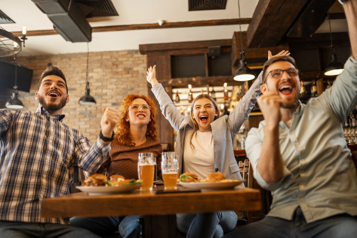 A group of people are sitting at a table in a restaurant with their arms in the air.