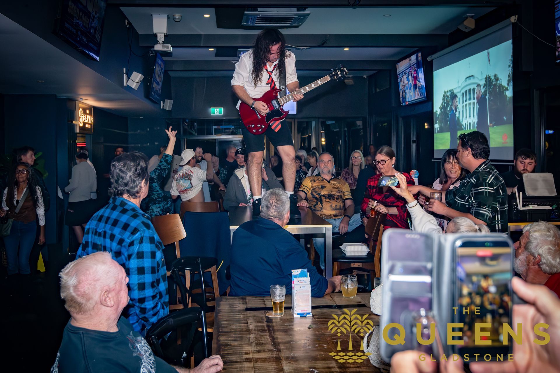 Drag performer on a table in a crowded bar, with patrons watching and clapping around her.