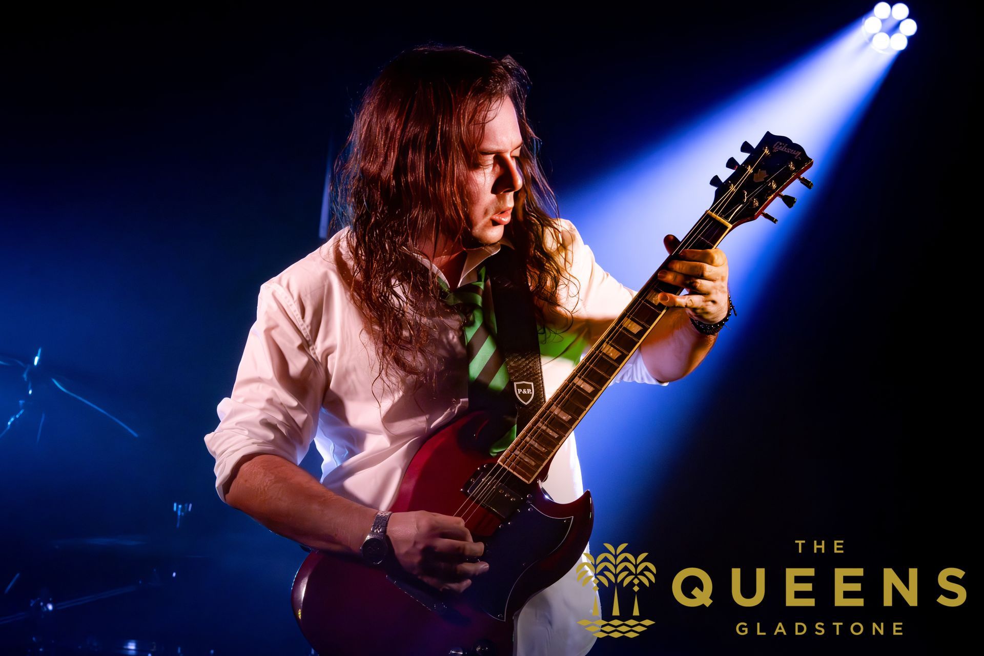 Guitarist performing on stage under blue spotlight, with The Queens logo and “Gladstone” text.