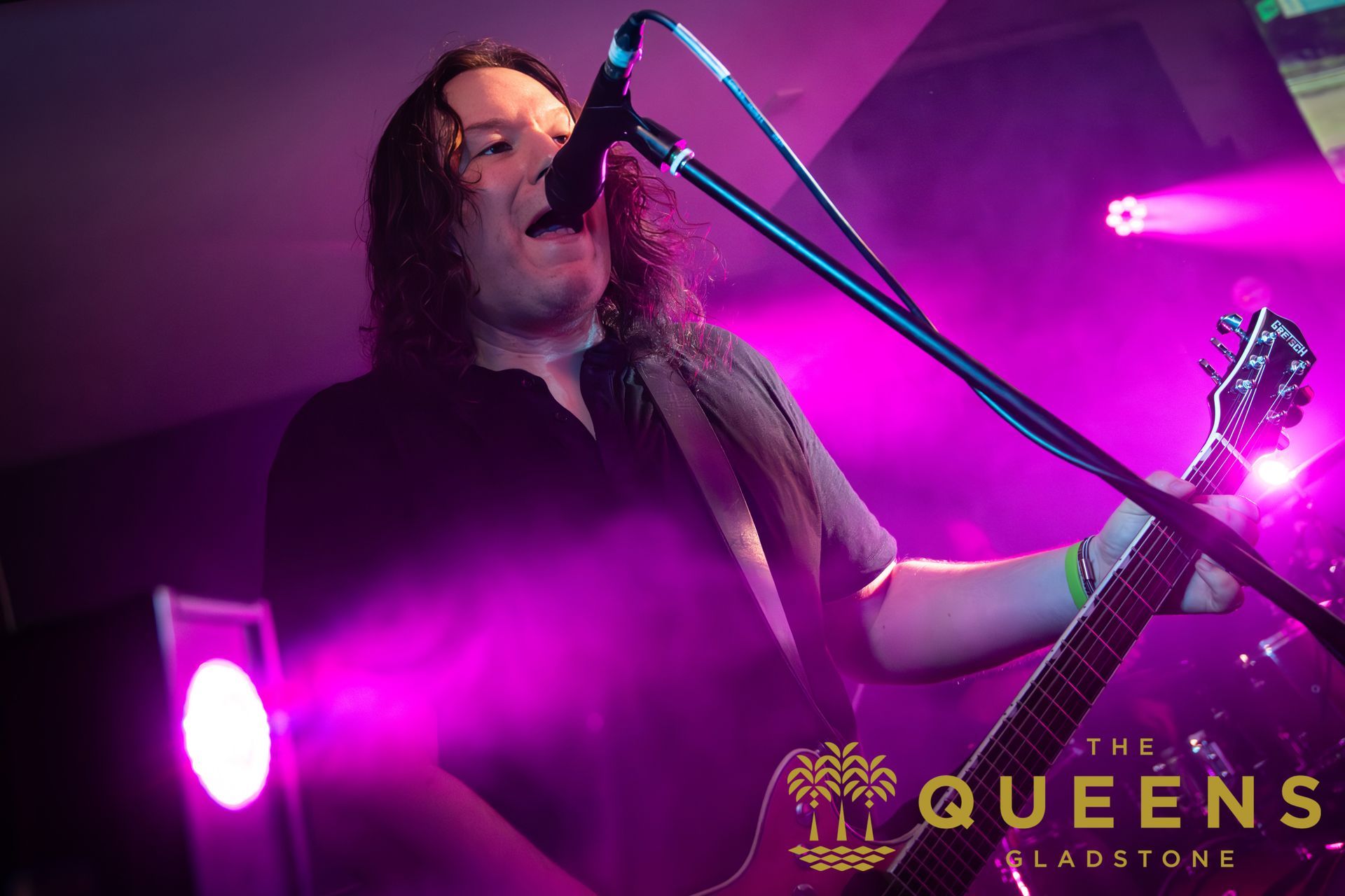 Singer performing on stage under purple lights, singing into a microphone with guitar in hand