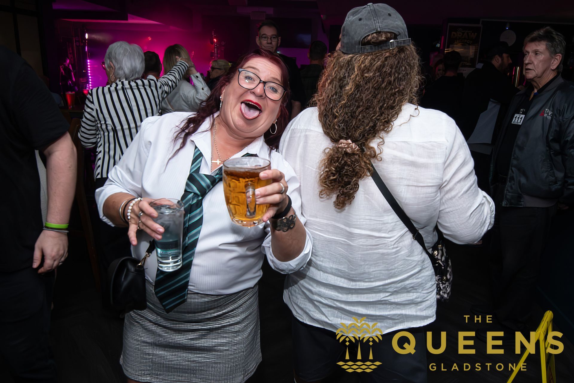 Woman in white shirt and striped skirt smiling with a drink at a nightclub, with a Queens Gladstone logo.