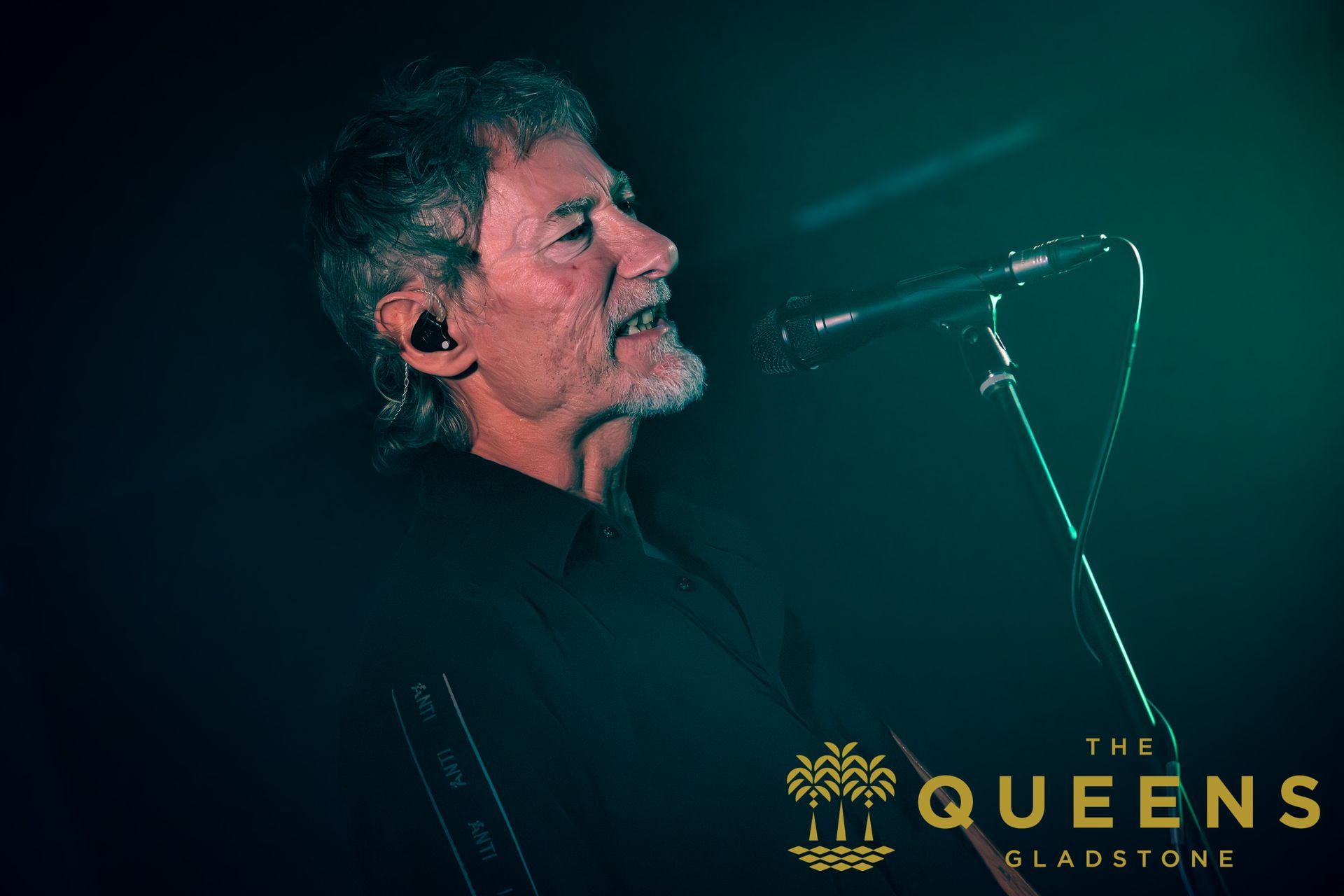 Singer performing on dark stage beside a microphone, with “The Queens Gladstone” logo at bottom right.