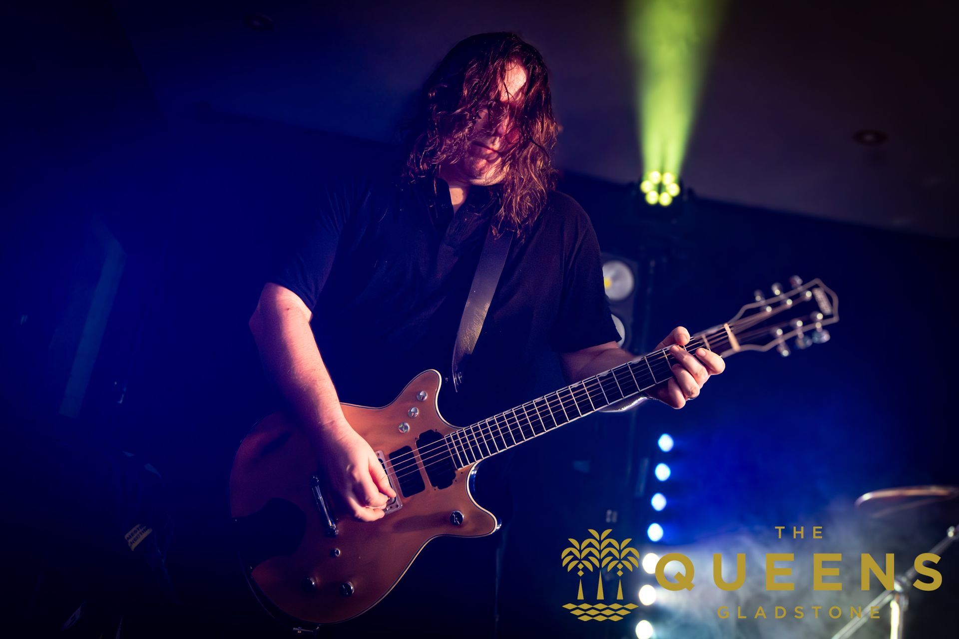 Guitarist performing on a dark stage under blue and yellow lights, with
