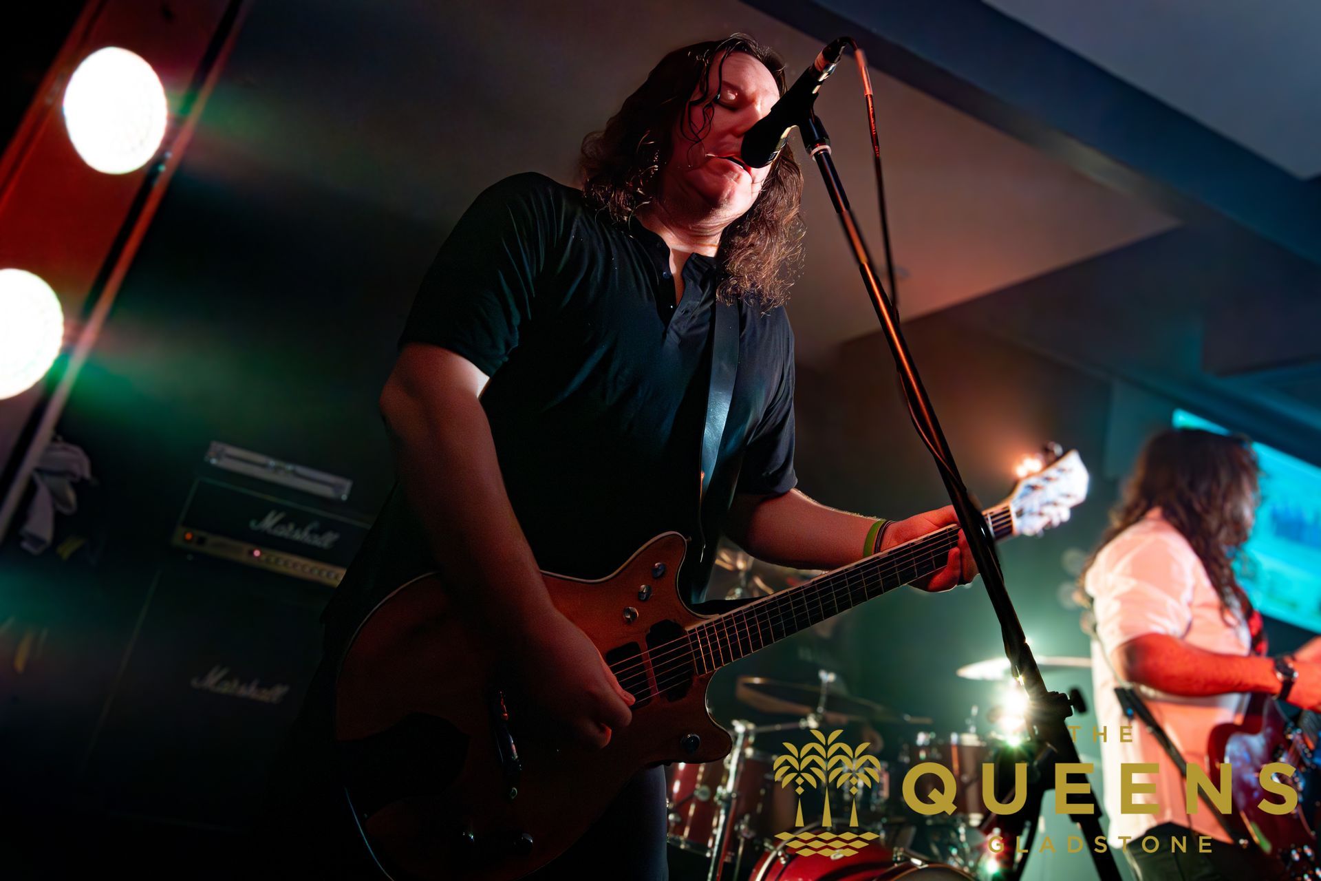 Band performing on stage under red and blue lights, guitarist in the foreground