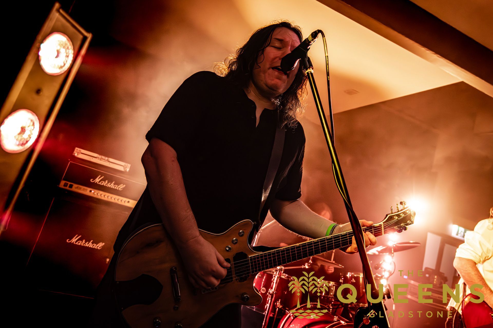 Musician singing and playing electric guitar onstage under warm orange lights