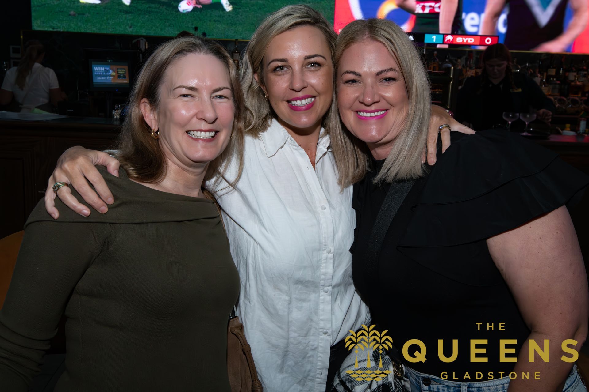 Three women smiling and posing together at The Queens gala event.