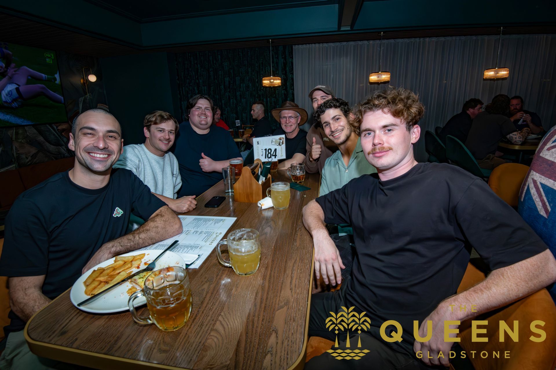 Friends seated at a restaurant table, smiling with drinks and plates in a dimly lit booth.