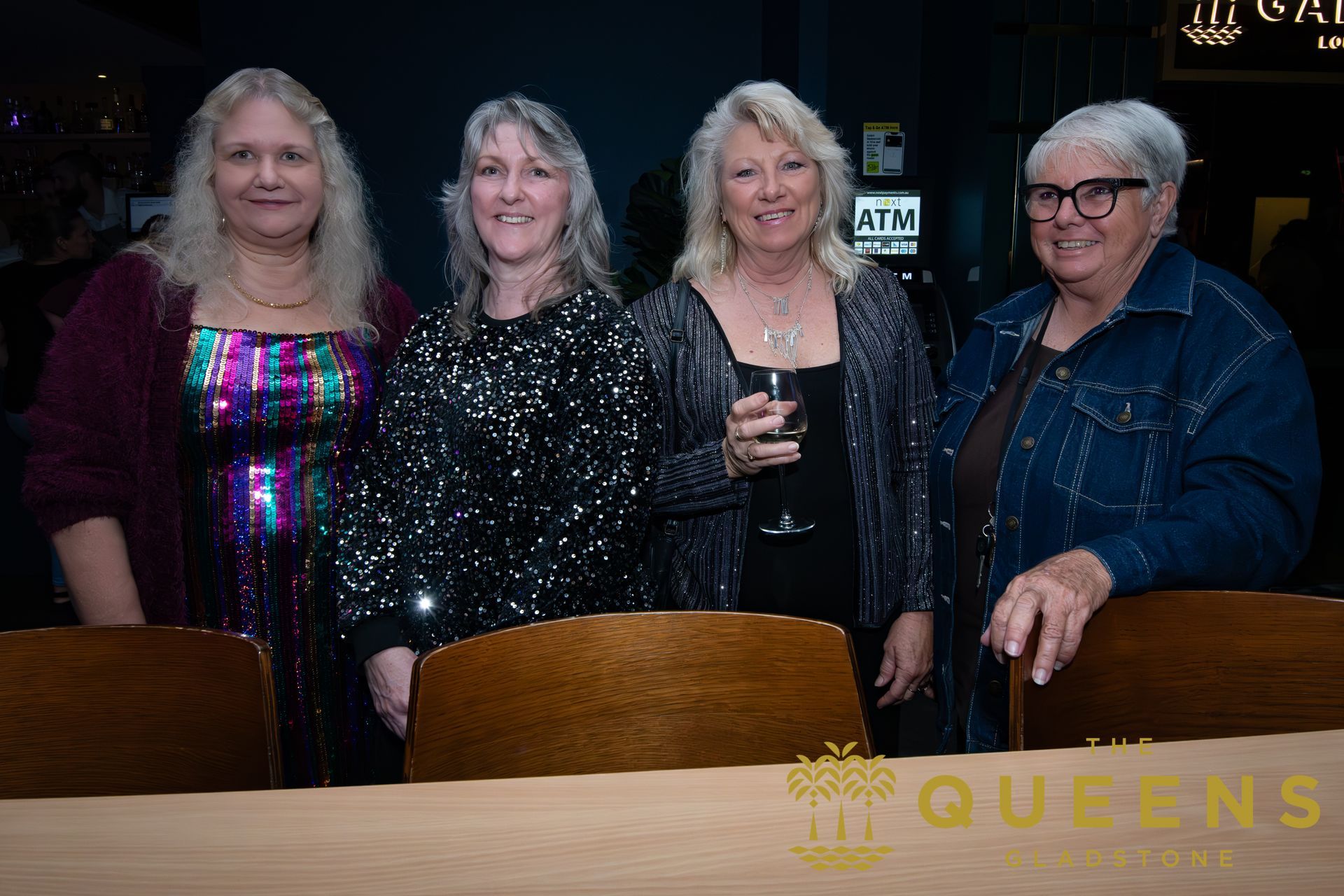 Four people standing behind a table, posing at an indoor event, with one holding a drink.