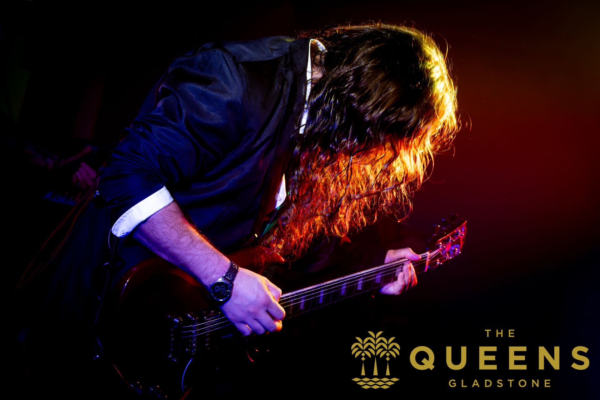 Long-haired guitarist on dark stage under red and purple lights, with