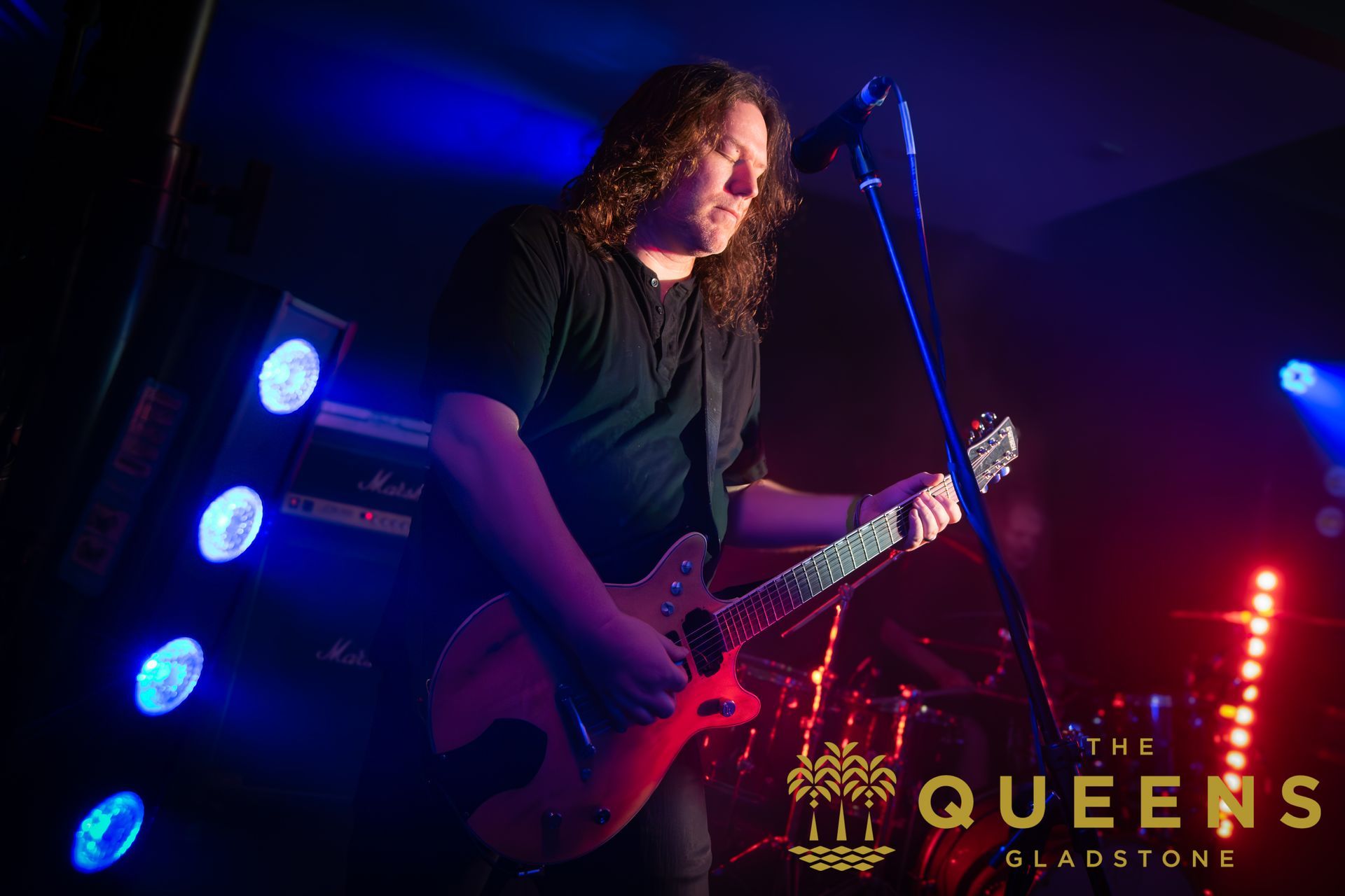 Guitarist performing on stage under blue and red lights at Queens Gladstone