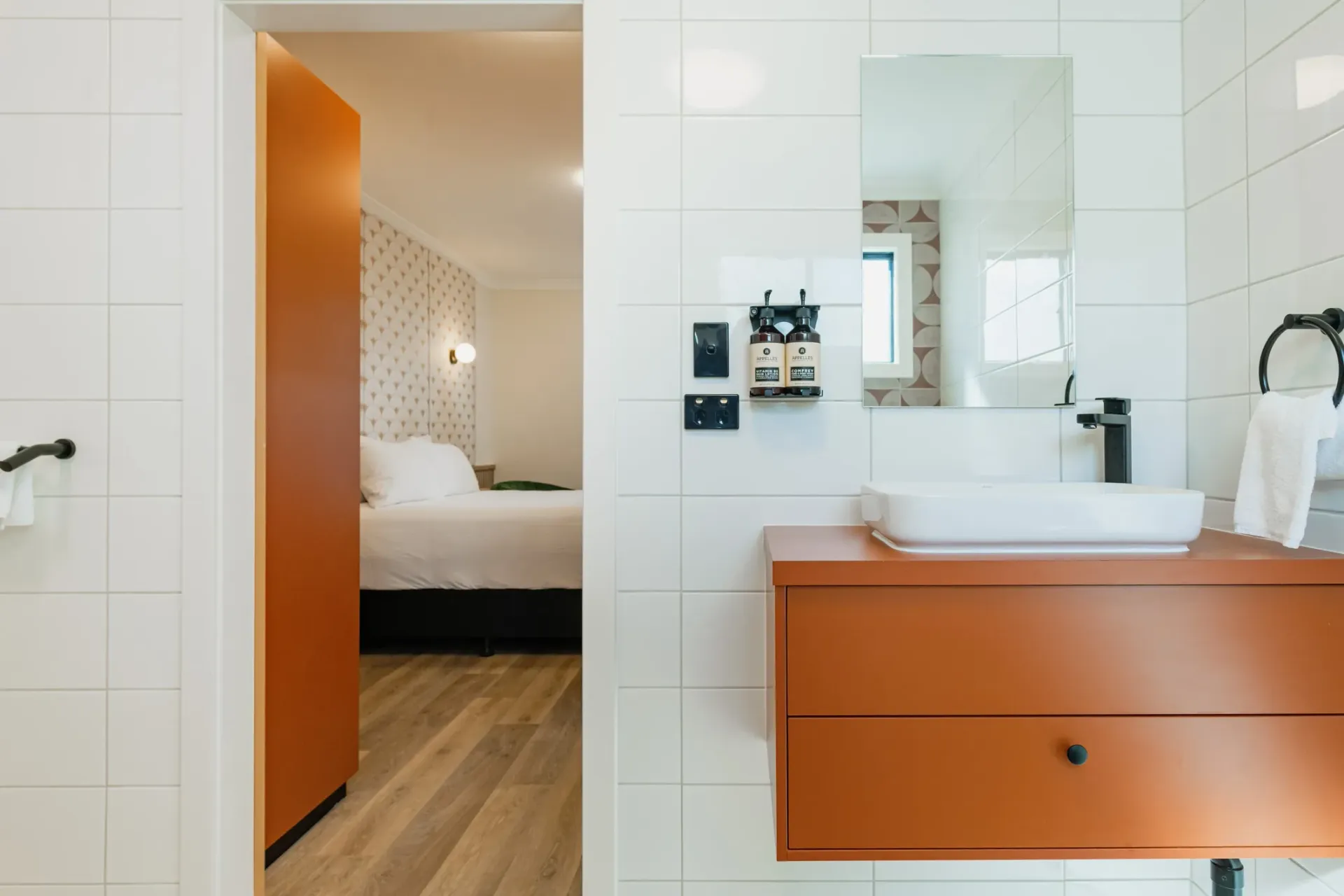 A bathroom with a sink , mirror , drawers and a door leading to a bedroom.