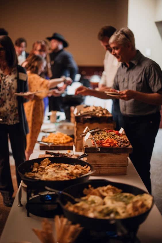 A group of people are standing around a table filled with food.