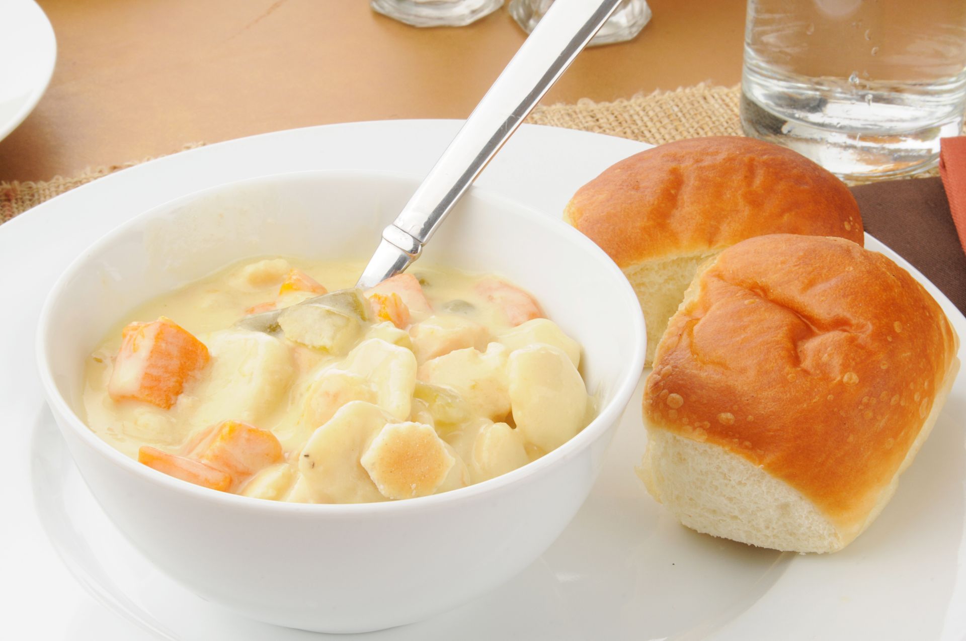 There is a bowl of soup and two rolls on a plate.