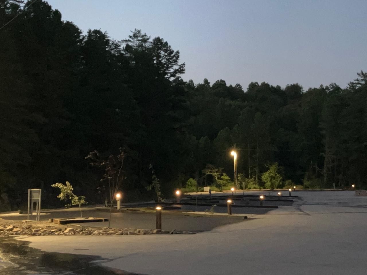 A camping area at dusk, with small lights illuminating the grounds and surrounding trees.