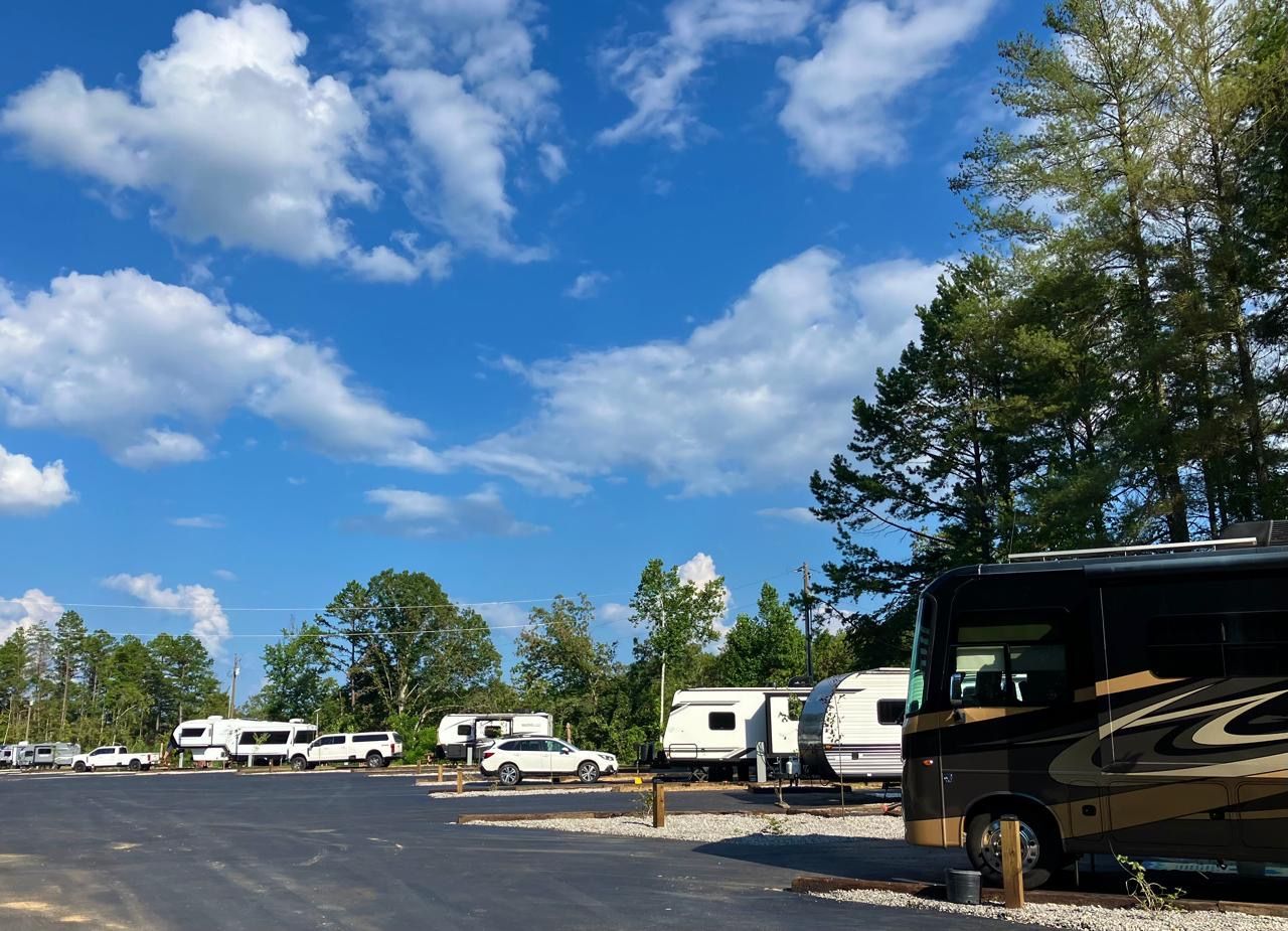 RV campground under a blue sky with white clouds; several RVs parked on asphalt.