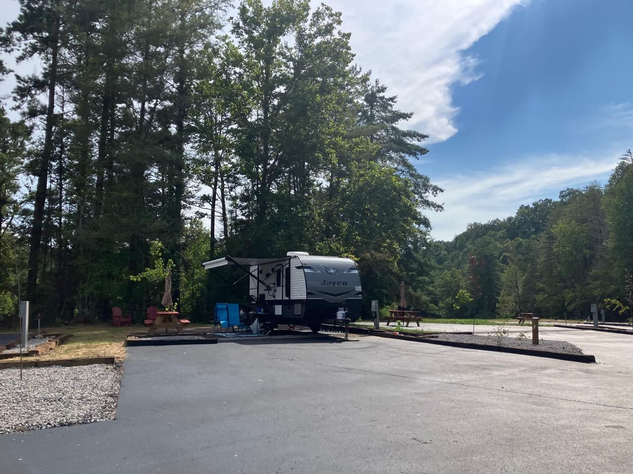 RV parked in a campsite with awning extended, surrounded by trees under a blue sky.