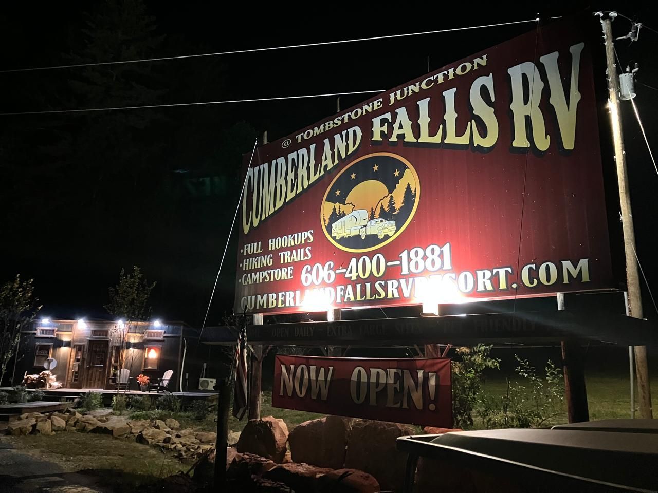 Sign for Cumberland Falls RV Resort at night, red, with lit-up office/store in the background, 