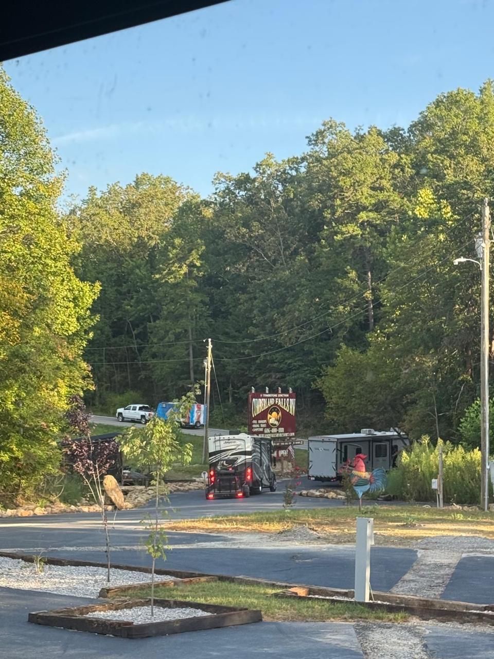 Construction site with a tractor, building, trees, and a sign against a backdrop of a treeline.