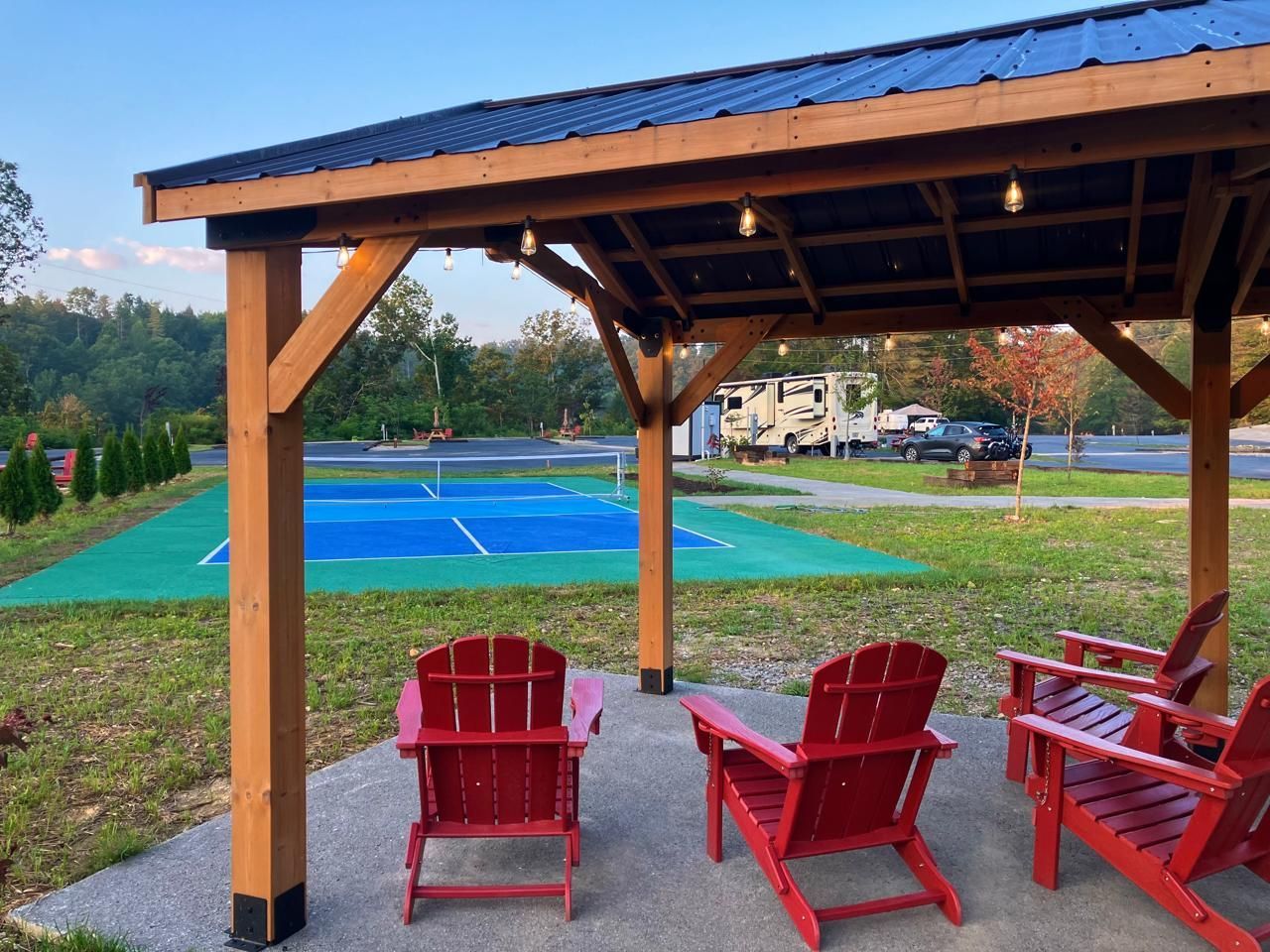 Red Adirondack chairs under a gazebo overlooking a pickleball court and RVs.