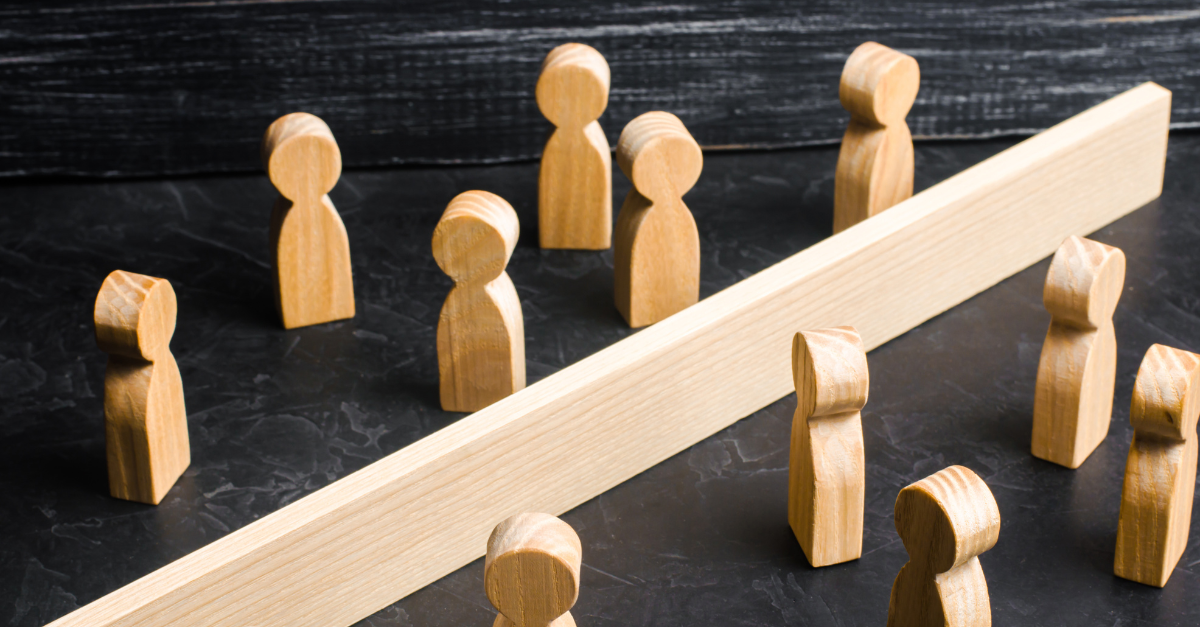 Wooden figurines divided by a barrier, symbolizing obstacles or separation between groups of people.