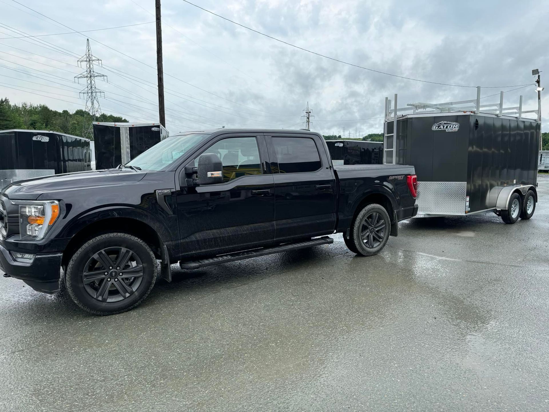 Une camionnette noire tracte une remorque sur une route mouillée.