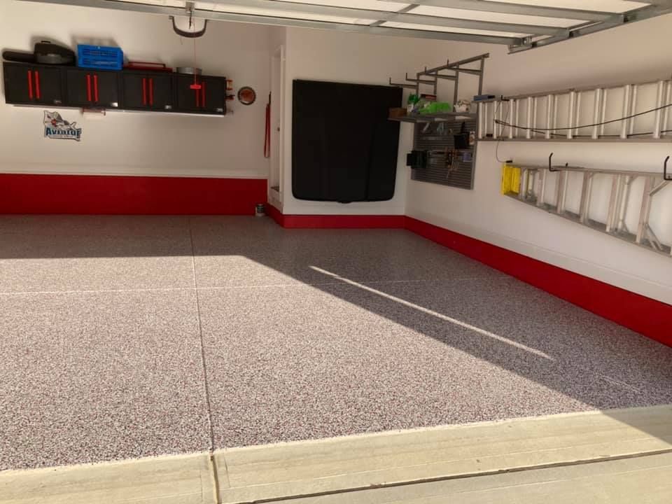 Clean, well-lit garage with speckled floor, red trim, and storage cabinets.