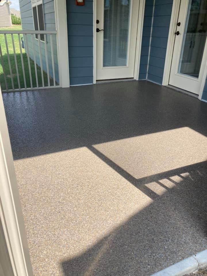 Exterior patio with speckled gray flooring, blue building, and white doors.