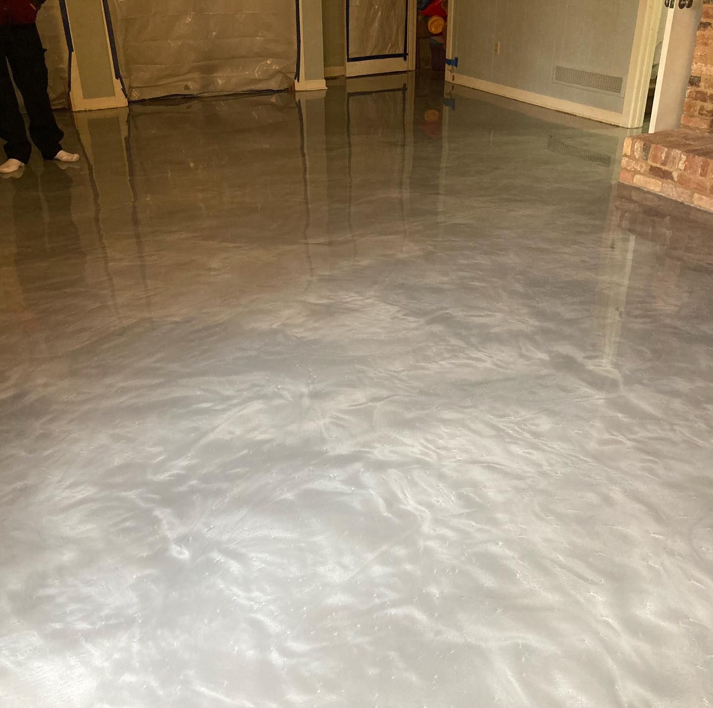 Glossy, silver-toned epoxy floor with light reflective streaks.  Room with beige walls and a brick column.
