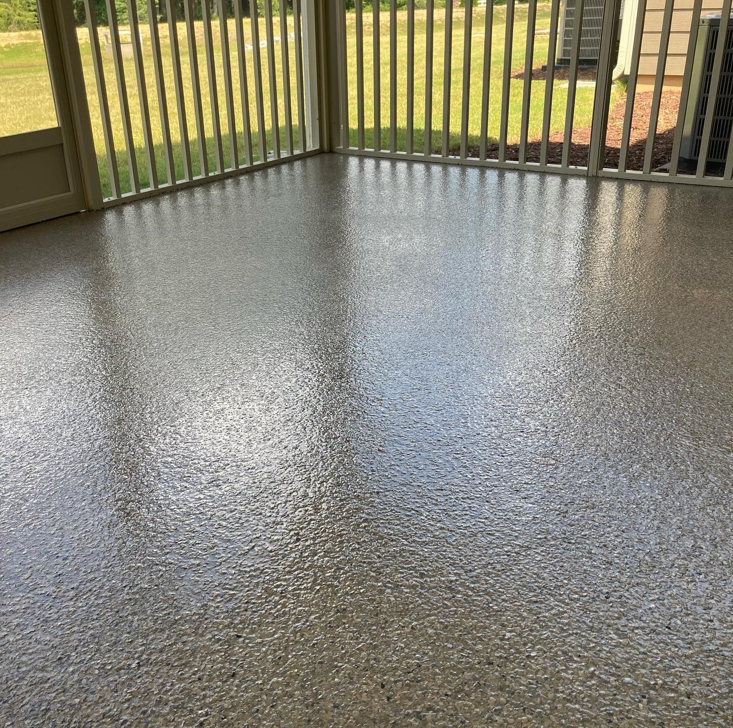 Screened-in porch with shiny, speckled gray floor. White railing and green grass visible through windows.