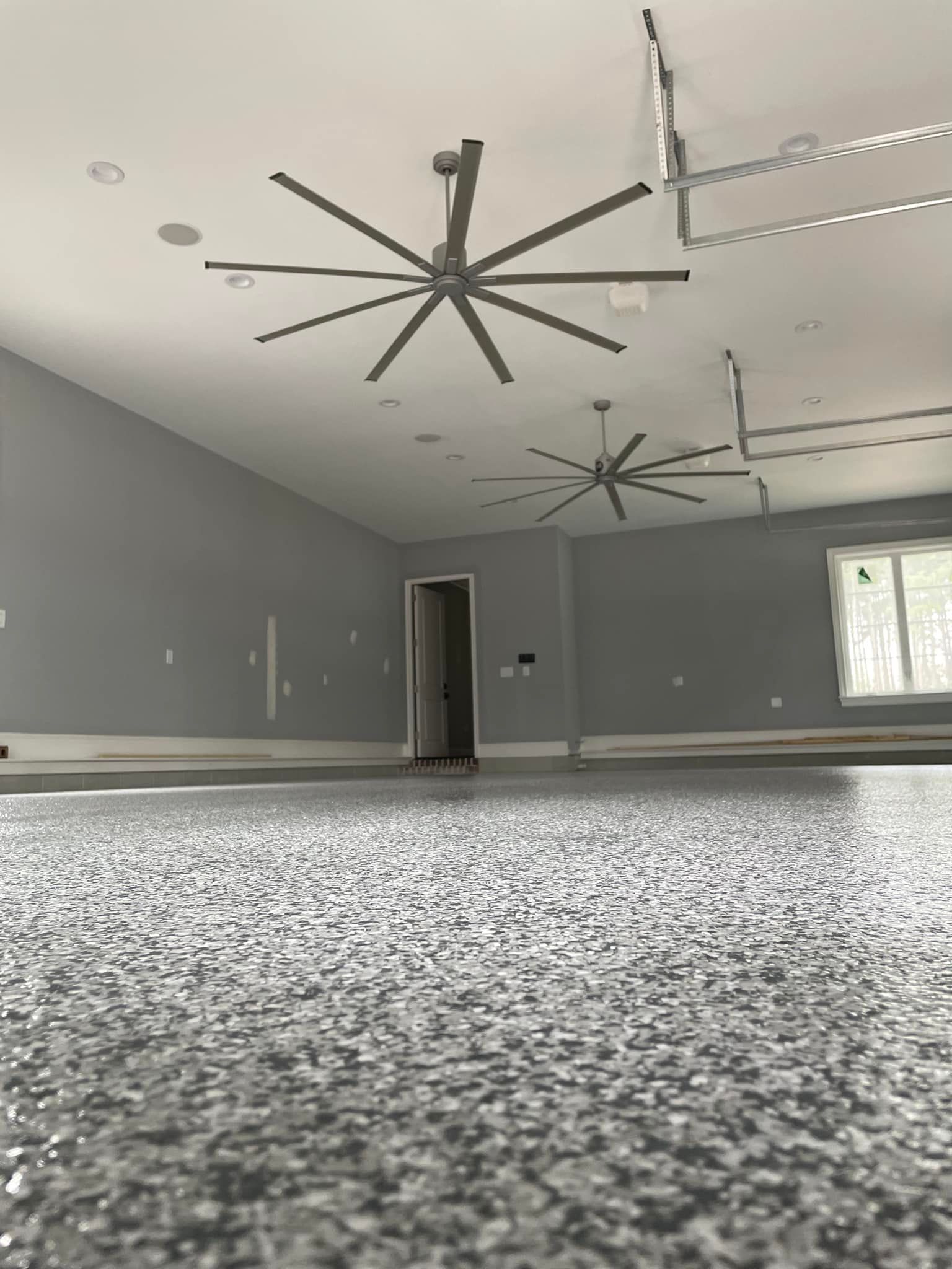 Large, open room with speckled floor, gray walls, two large ceiling fans, and a doorway.