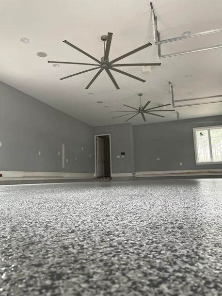 Spacious room with gray walls and a speckled floor. Two large ceiling fans are visible.