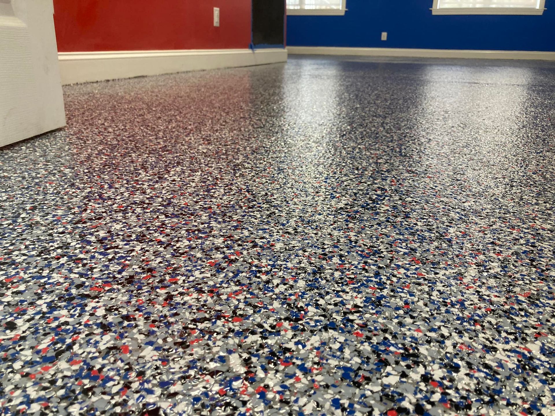 Epoxy garage floor with blue, red, white, and gray flakes, reflecting the room's walls.