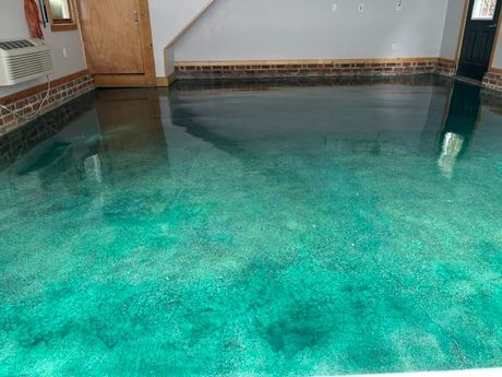 Epoxy-coated garage floor, teal green with reflective areas, near a wooden door and brick walls.