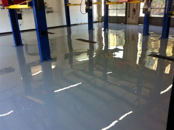 Gray, glossy epoxy floor in a garage with blue car lifts, reflecting overhead lighting.