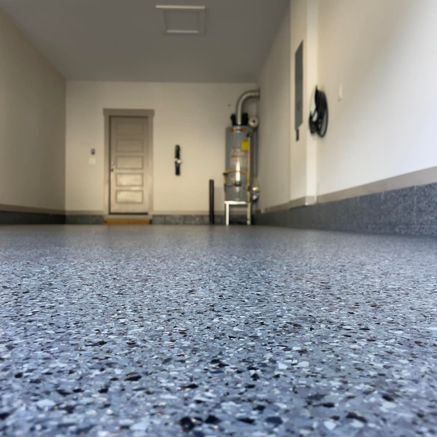 Garage interior with a speckled epoxy floor, white walls, and a door at the end.