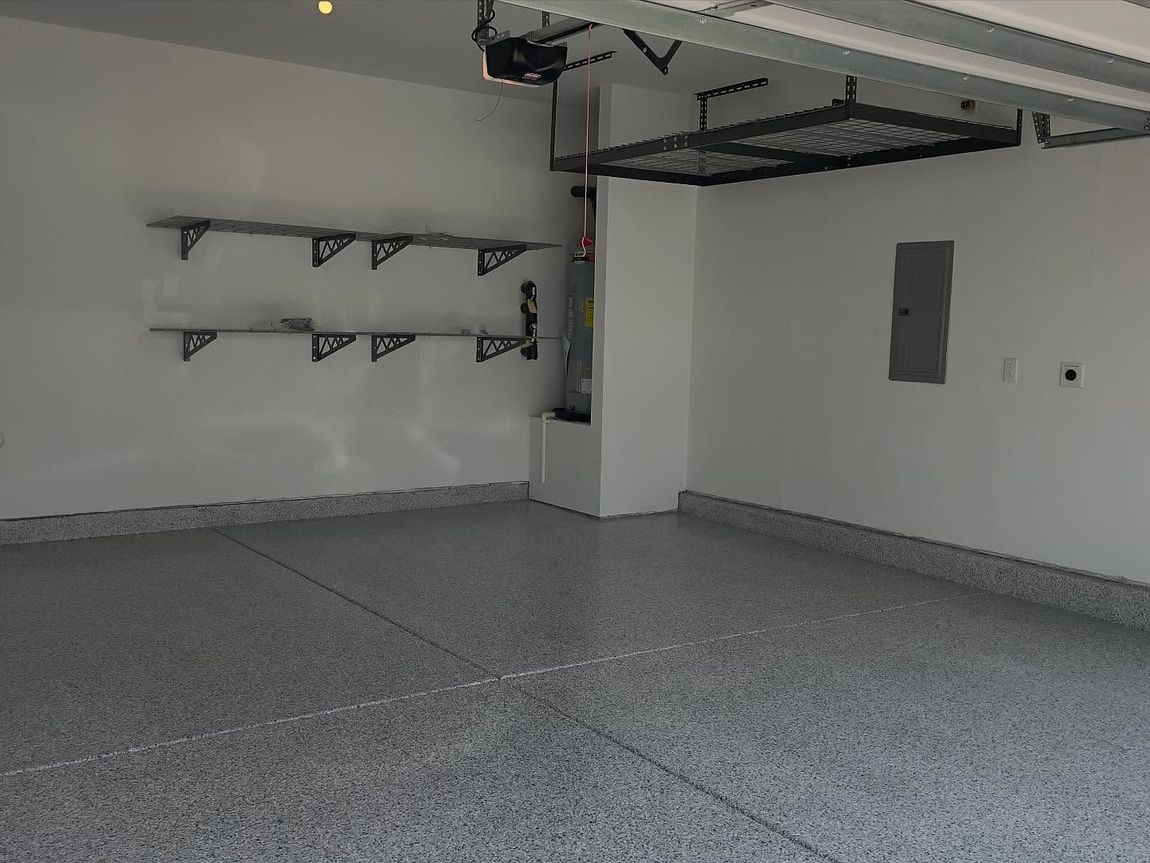 Empty garage with gray speckled floor, white walls, storage shelves, and overhead storage.
