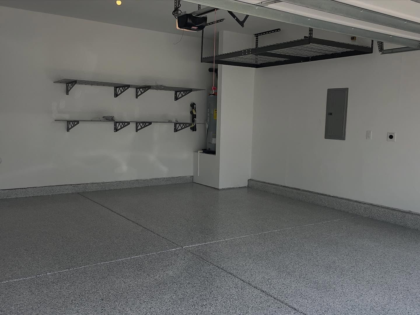 Empty garage with gray speckled floor, white walls, storage shelves, and overhead storage.