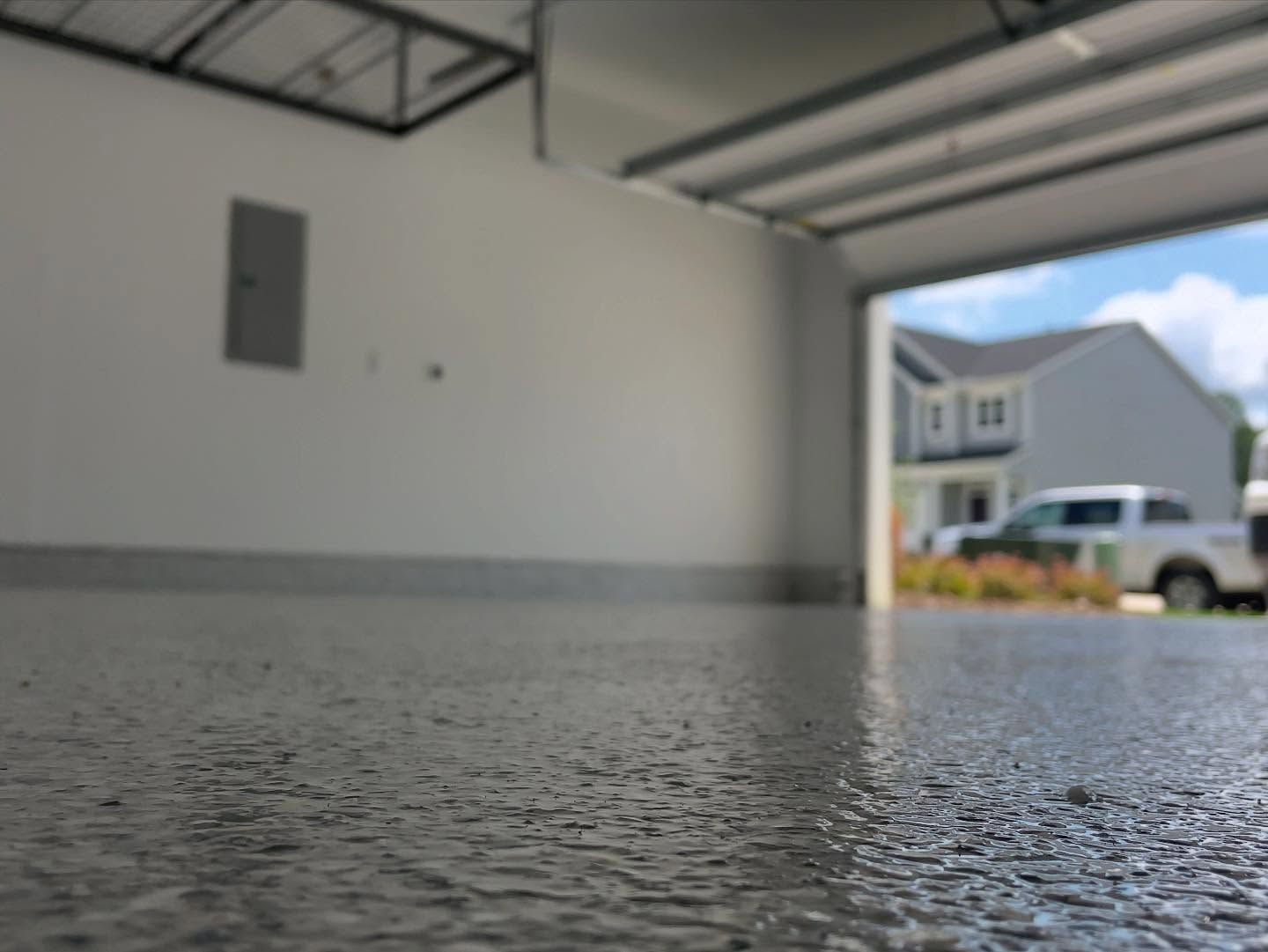 Low-angle view of a garage with a textured, glossy floor, open to a sunny day outside.