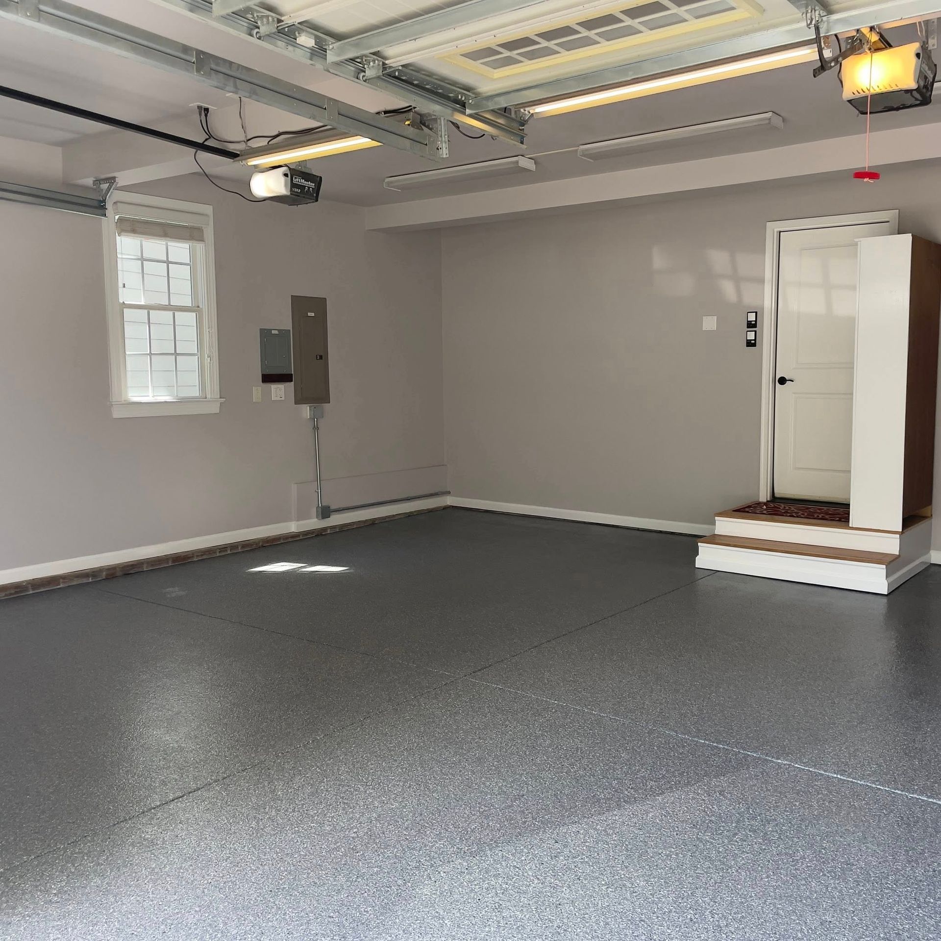 Empty garage with gray epoxy floor, white door, window, and electrical panel.