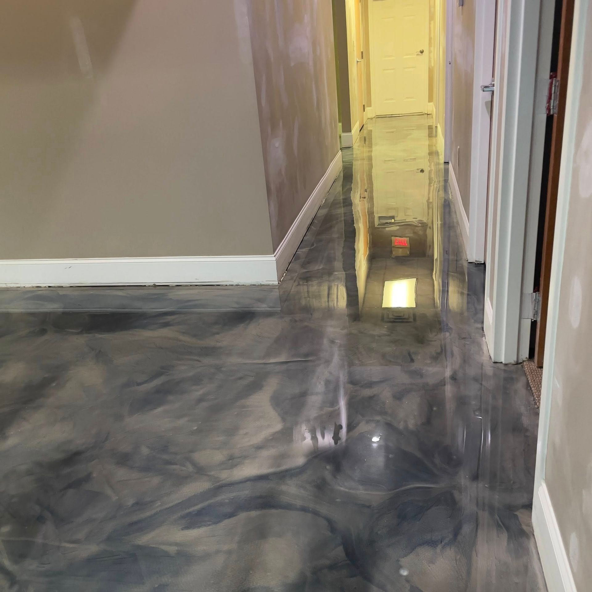 Shiny, marbled epoxy floor reflecting light in a hallway. Beige walls, white trim.