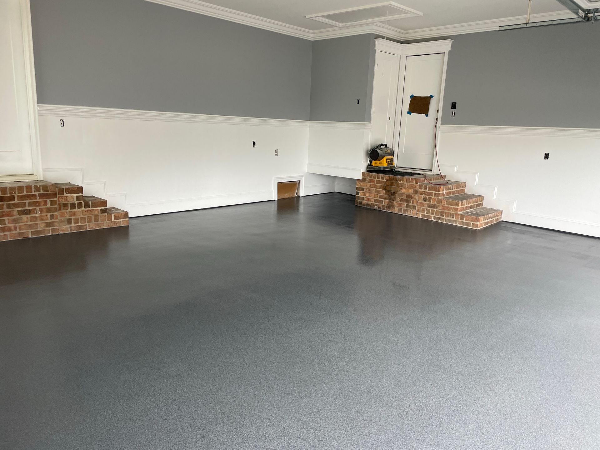 Grey epoxy-coated garage floor with white wainscoting and grey upper walls. Brick step features on either side.
