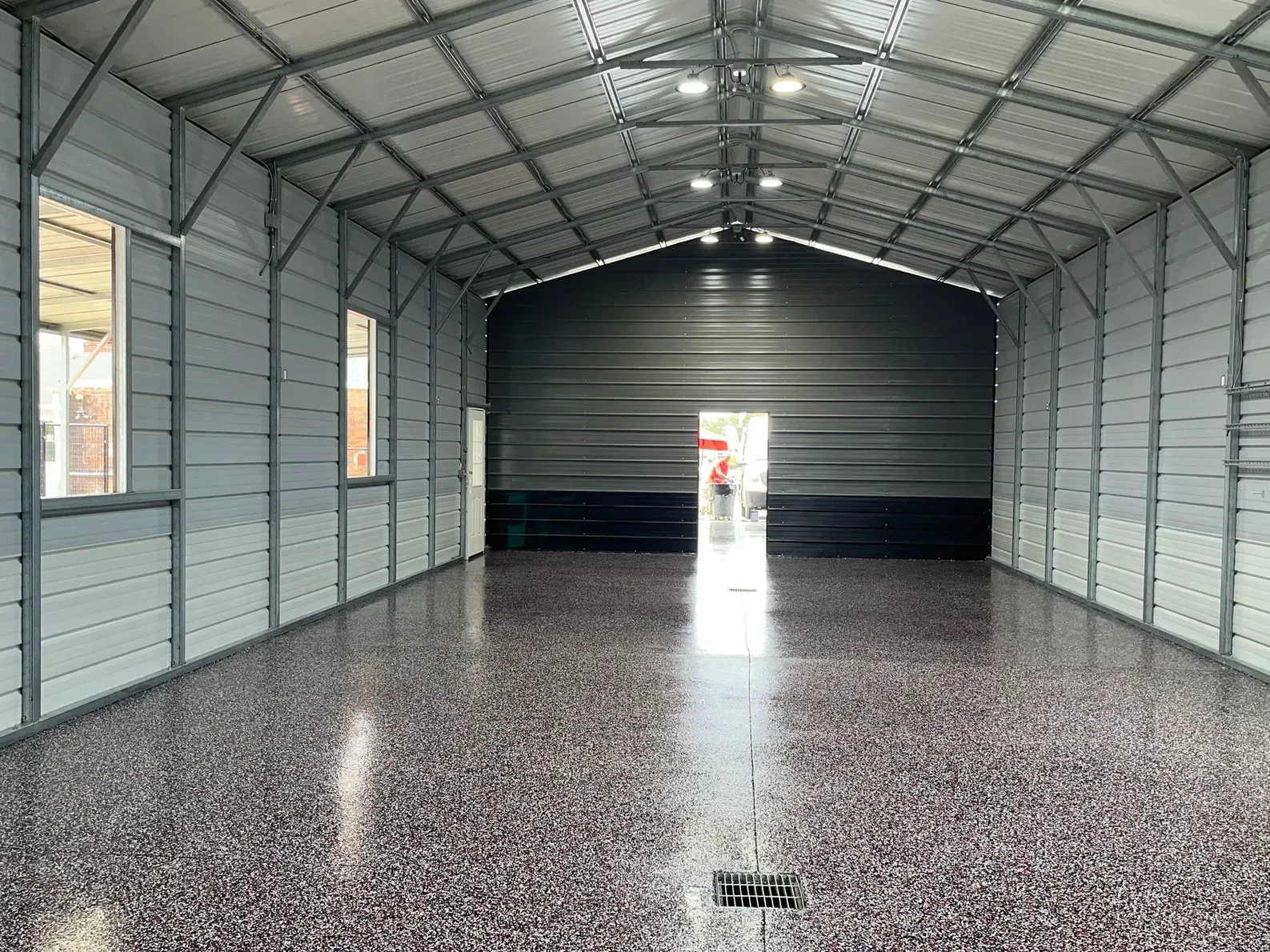 Interior of a large gray metal building with a speckled floor and open door at the end.
