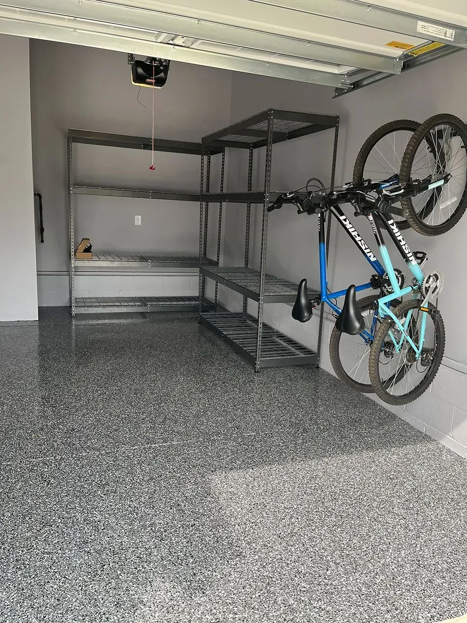 Garage interior with gray epoxy flooring, metal shelving, and two bicycles mounted on a wall.