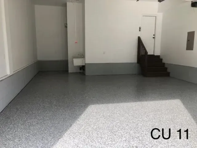 Empty garage with gray speckled floor, white walls, and stairs.