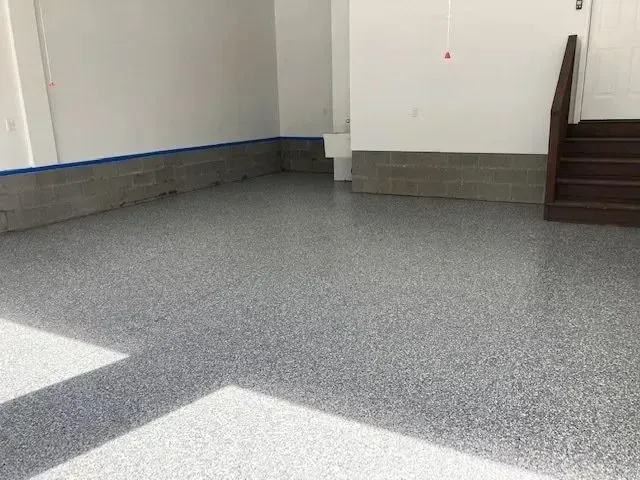 A garage with a gray speckled epoxy floor, white walls, and a set of wooden stairs.