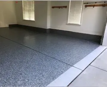 Garage with a gray speckled epoxy floor and white walls. Two windows with blinds.