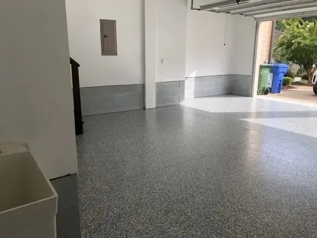 Finished gray epoxy garage floor, light reflecting. Walls are white, with gray base.