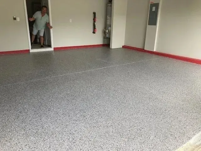 Garage with gray speckled epoxy floor and red trim. Man in doorway.